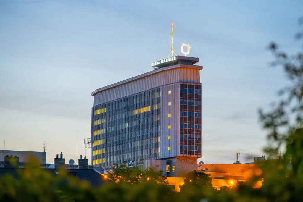 Vysoká moderní budova, před ní je sídliště nižších paneláků a rodinných domů