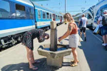 Dvě ženy se ochlazují na vlakovém nádraží u pítka s vodou