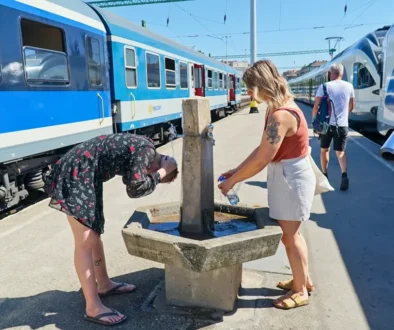 Dvě ženy se ochlazují na vlakovém nádraží u pítka s vodou