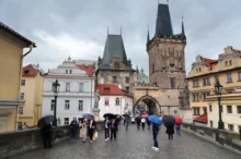 Lidé pod deštníky jdou po Karlově mostě v Praze