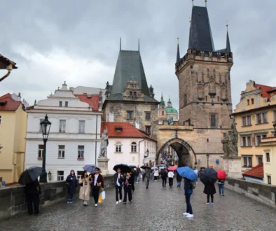 Lidé pod deštníky jdou po Karlově mostě v Praze