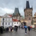 Lidé pod deštníky jdou po Karlově mostě v Praze