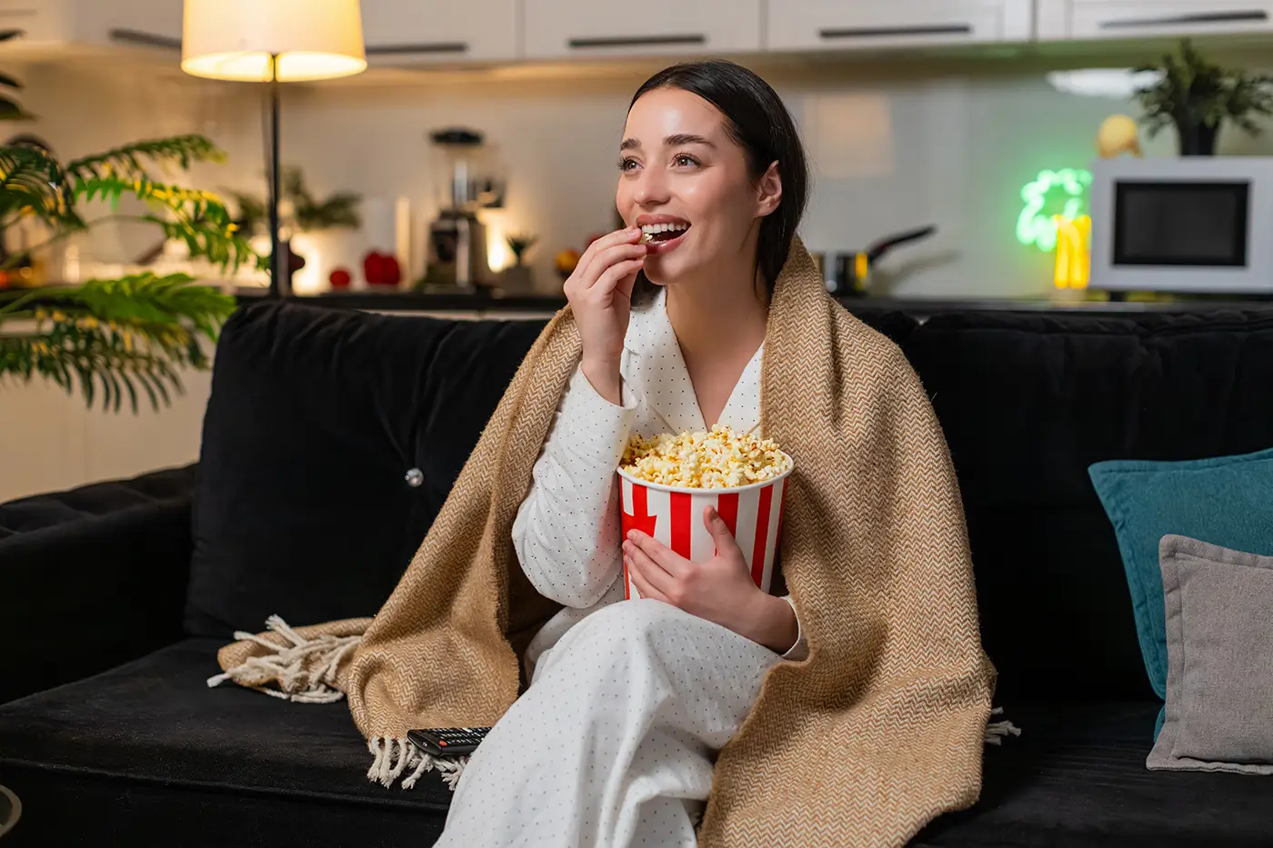 shutterstock_2716548021 - VIPshow Žena je přikrytá dekou, jí popcorn a kouká na televizi