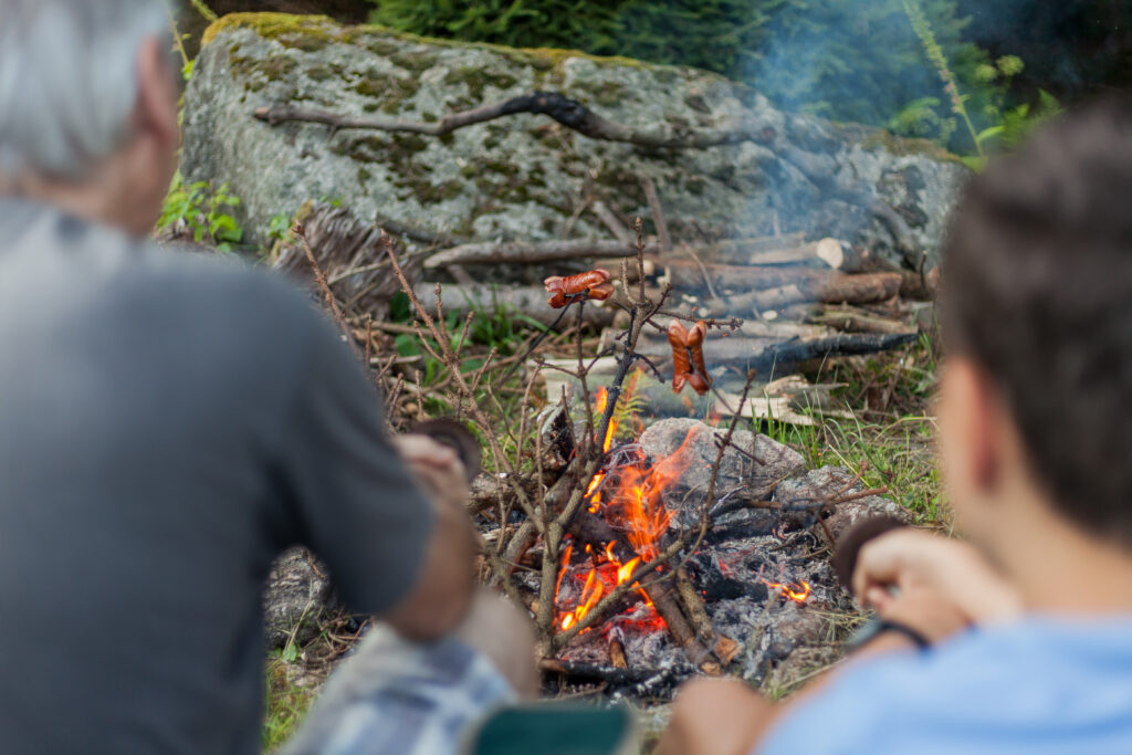 CzechRepublic-July25BarbecueJuly252017In - VIPshow Šedovlasý muž a malý chlapec drží tyčky s buřty nad rozdělaným ohněm v přírodě
