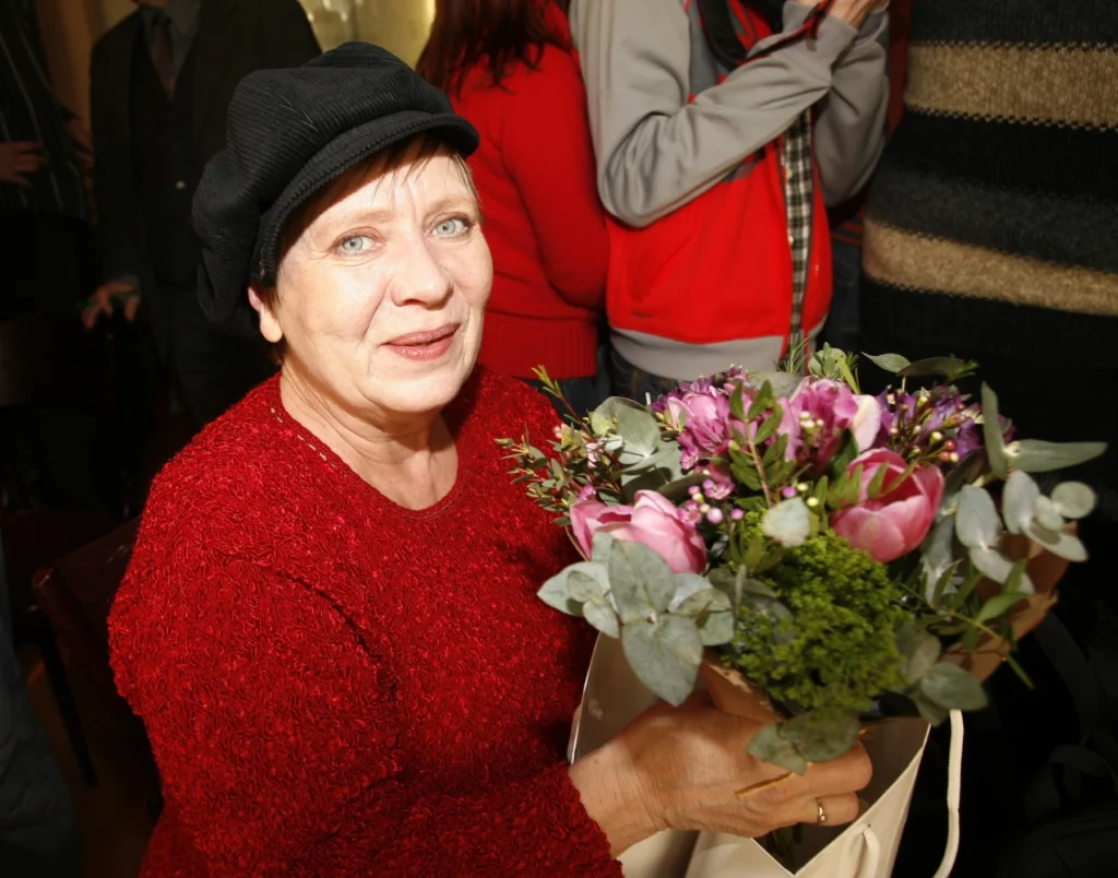profimedia-0020127459 - VIPshow Starší dáma v červeném svetru a černé bekovce s kyticí květů se usmívá do objektivu