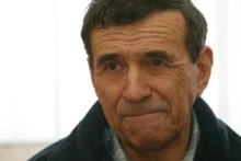 Muž s tmavými vlasy a v tmavé bundě se dívá do dáli
