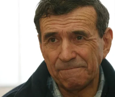 Muž s tmavými vlasy a v tmavé bundě se dívá do dáli