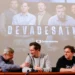 Tři muži sedí u stolu v sále, za nimi je velké plátno a na něm svítí fotografie s nápisem Devadesátky