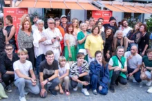 Velká skupina lidí, herců, za nimi jsou obchůdky a nápisy Ulice