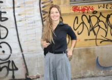 Mladá žena stojí před počmáranou zdí a usmívá se do kamery
