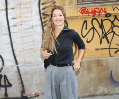 Mladá žena stojí před počmáranou zdí a usmívá se do kamery