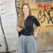 Mladá žena stojí před počmáranou zdí a usmívá se do kamery