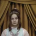 Dívka oblečená jako princezna se trochu ustrašeně rozhlíží, kam vstoupila, za ní jsou těžké, žluté závěsy