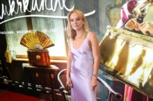 Žena ve světlých šatech stojí před filmovým plakátem a nechává se fotit