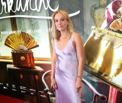 Žena ve světlých šatech stojí před filmovým plakátem a nechává se fotit