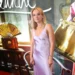 Žena ve světlých šatech stojí před filmovým plakátem a nechává se fotit