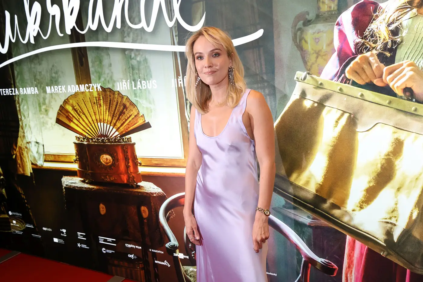 Žena ve světlých šatech stojí před filmovým plakátem a nechává se fotit