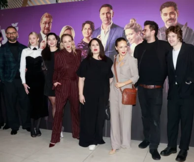 Skupina lidí ve večerních šatech před plátnem, na které jsou také oni, ale ve filmu