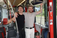 Dva mladí muži se drží za madla v tramvaji a smějí se