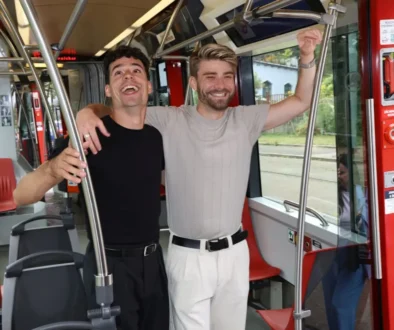 Dva mladí muži se drží za madla v tramvaji a smějí se