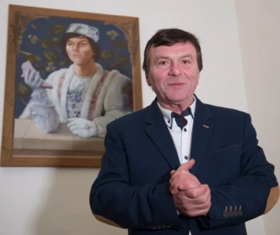 Muž v modrém obleku, za ním je obraz se stejným mužem, ale mladším, v pohádkovém převleku prince