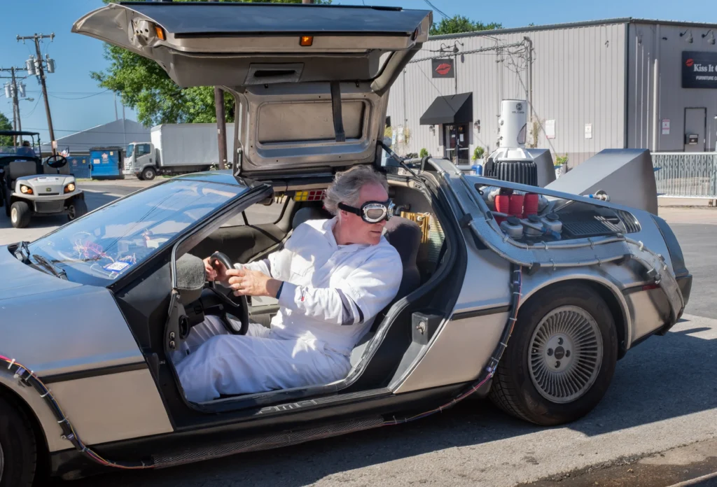 Futuristické auto a v něm muž v podivných brýlích a bílé kombinéze