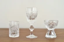 Crystal glassware set on a wooden table, featuring a tall center goblet and patterned cut-glass tumblers on both sides.