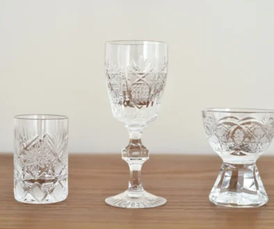 Crystal glassware set on a wooden table, featuring a tall center goblet and patterned cut-glass tumblers on both sides.