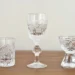 Crystal glassware set on a wooden table, featuring a tall center goblet and patterned cut-glass tumblers on both sides.