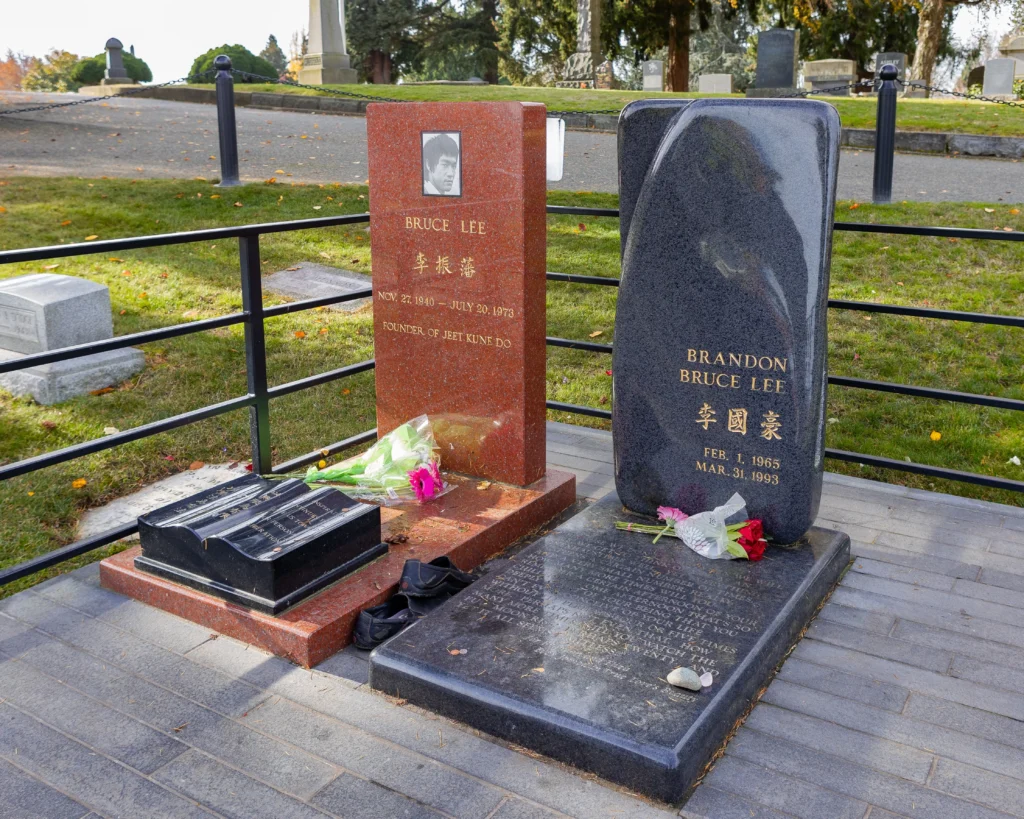Dva hroby vedle sebe, jeden z červené, druhý šedé žuly nebo mramoru, na jednom je jméno Bruce Lee, na druhé Brandon Lee
