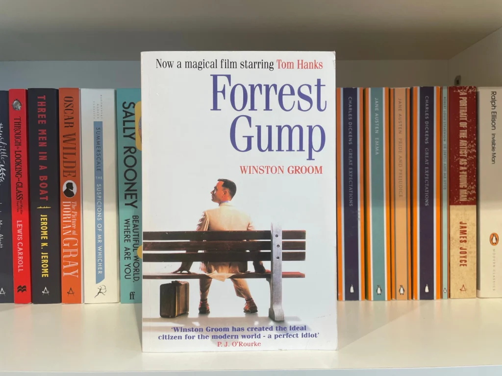 Kniha Forrest Gump v knihovně, na přebalu sedí Tom Hanks s kufříkem na lavičce