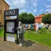Louka před kinem, na ní je cedule s nápisem Kino a několik plastik ve tvaru srdce s různými motivy