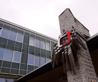 Low-angle view of a modern glass-fronted building with a stone tower and a red sculptural accent