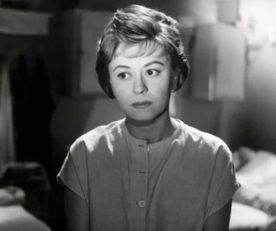 Black-and-white photo of a woman with short hair and a buttoned blouse, looking off to the side in a dim indoor setting.