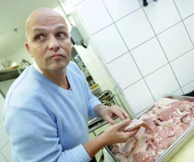 Muž bez vlasů stojí v kuchyni a sklání se nad tác s masem