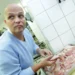 Muž bez vlasů stojí v kuchyni a sklání se nad tác s masem
