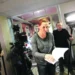 Žena v tmavém tričku a se zrzavými vlasy drží v ruce svázané papíry a listuje v nich