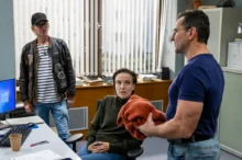 Nad ženou, která sedí v kanceláři na židli, stojí dva muži