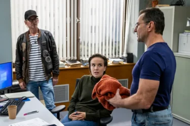 Nad ženou, která sedí v kanceláři na židli, stojí dva muži