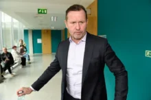 Muž v obleku a bílé košili se nachází na chodbě a je v pohybu