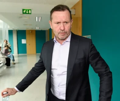 Muž v obleku a bílé košili se nachází na chodbě a je v pohybu