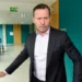 Muž v obleku a bílé košili se nachází na chodbě a je v pohybu