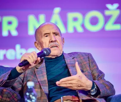 Starší muž bez vlasů sedí v křesle a mluví do mikrofonu