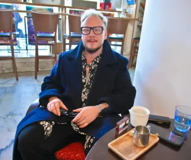 Mladý muž sedí v křesle, má na nose brýle a usmívá se