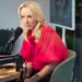 Mladá žena s blond vlasy a v červeném tričku sedí v křesle a mluví do mikrofonu