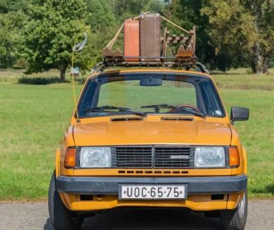 Staré žluté auto má na střeše přivázané kufry
