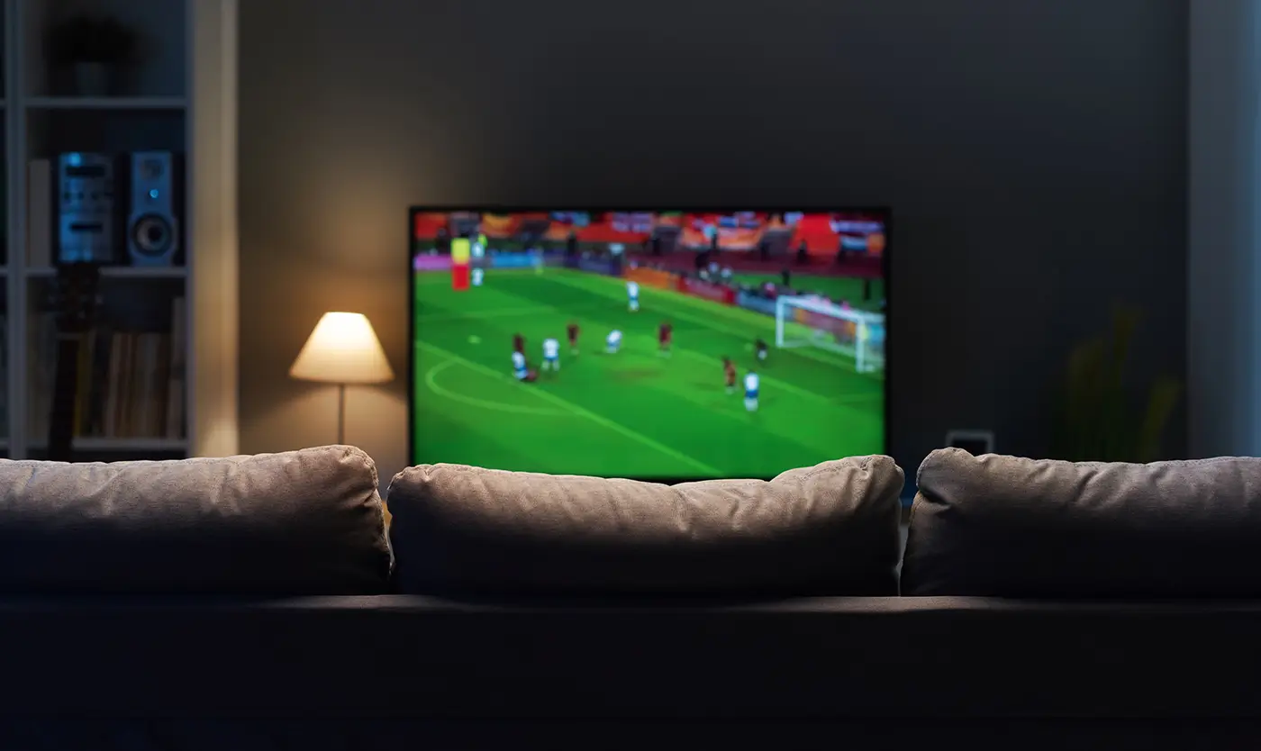 shutterstock_2171946833 - VIPshow V popředí je gauč a za ním je puštěná televize, na které běží fotbalové utkání
