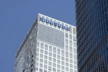 Vysoká moderní budova, nad ní modré nebe, na budově je nápis Samsung