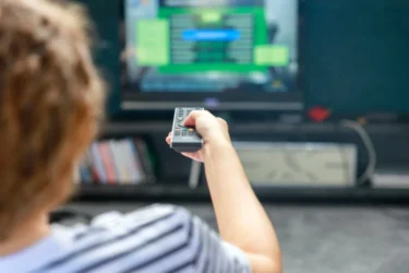 Osoba v pruhovaném tričku drží televizní ovladač