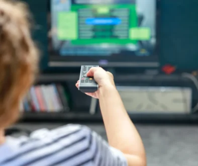 Osoba v pruhovaném tričku drží televizní ovladač